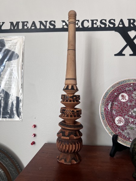 Tall carved wooden artefact with patterned rings on a shelf beside a decorated plate.