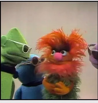 Colorful puppet characters, including an orange-haired character at the center.