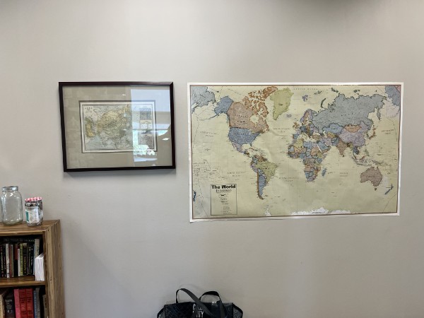 World map and smaller framed map on a wall beside a bookshelf.