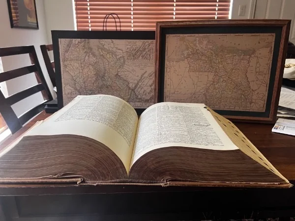 An open dictionary and framed maps arranged on a table.