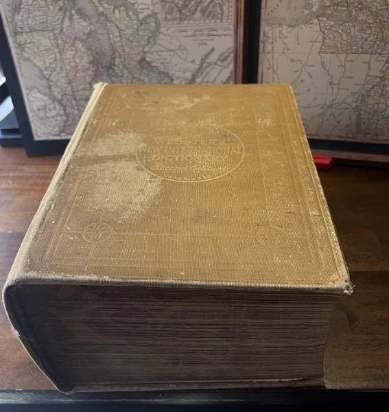 Webster’s New International Dictionary displayed in front of framed maps.