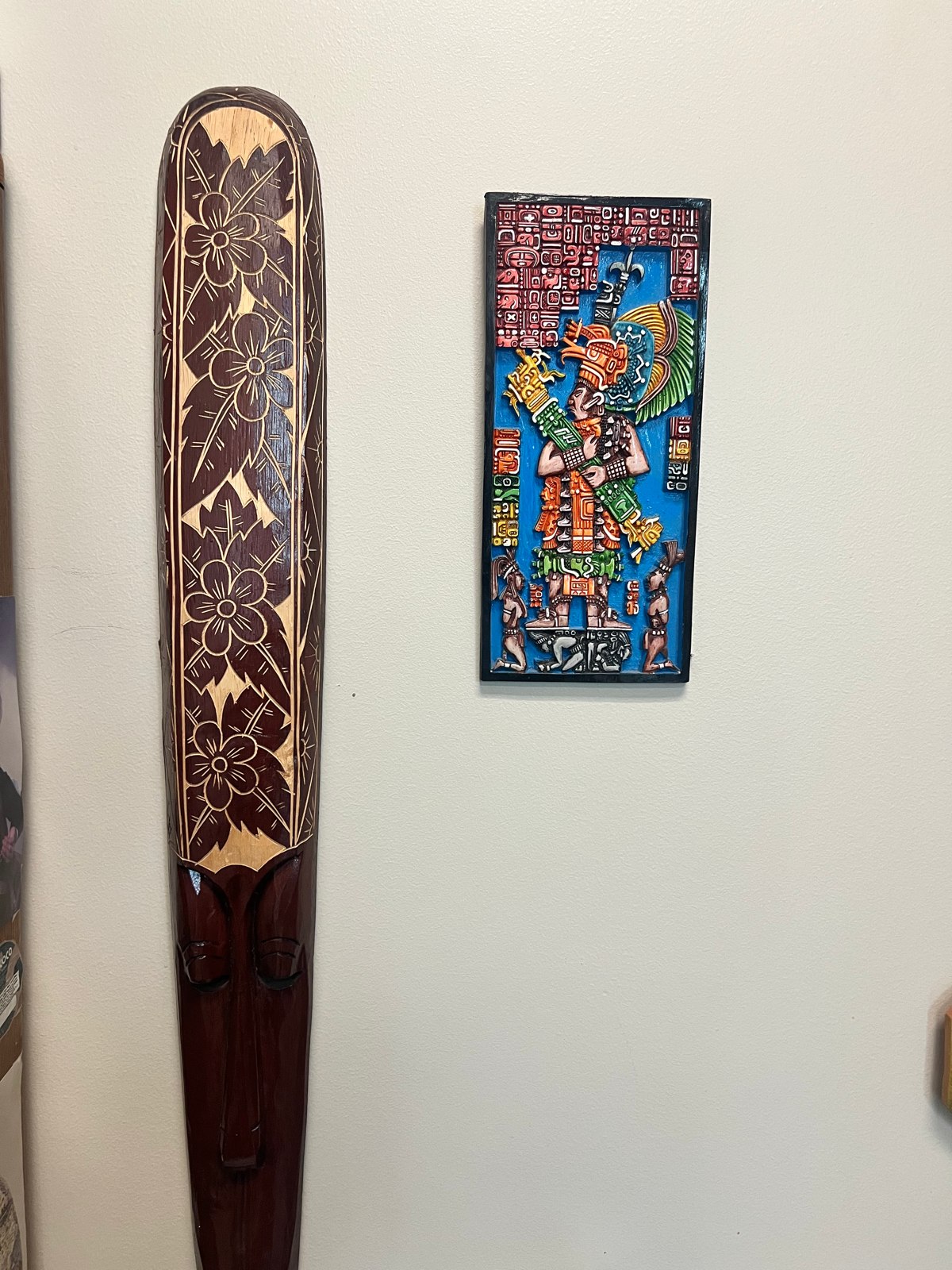 A long decorated wooden object and a colorful rectangular artwork displayed on a wall.